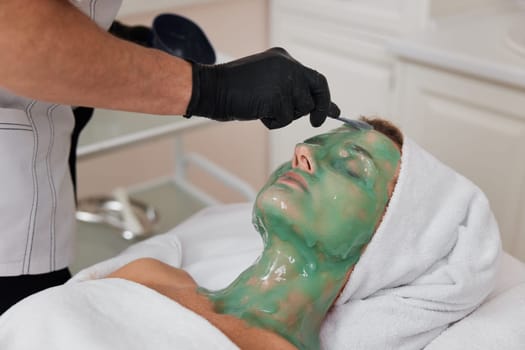 beautician applies green alginate mask to the face of beautiful woman in the spa salon. spa treatments