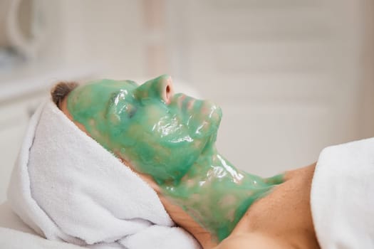 beautiful woman with green alginate mask on face in the spa salon. close-up