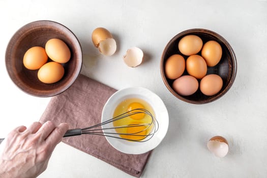A woman's hand is beating eggs with a whisk on the kitchen table. Top view.