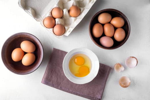 View from above brown chicken eggs in a cardboard packing container, and in a bowl on a table .