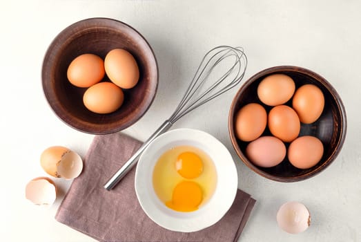 Top view brown chicken eggs in a bowl on the table with a whisk to beat the eggs.