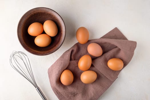 View from above brown chicken eggs in a bowl on a table with a whisk to beat the eggs.