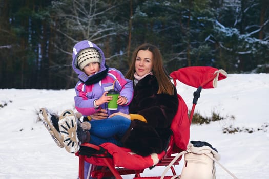 a woman in relation to her child or children. Satisfied mother with a child on a sled with a red plaid in the winter forest.