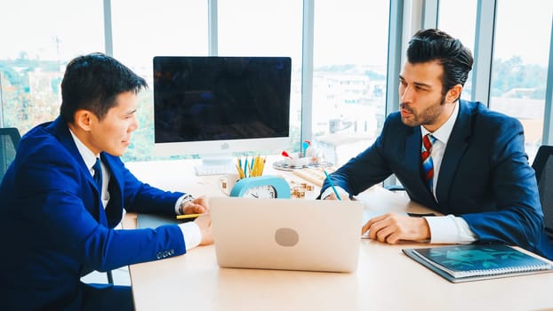 Two business people talk project strategy at office meeting room. Businessman discuss project planning with colleague at modern workplace while having conversation and advice on financial report. Jivy