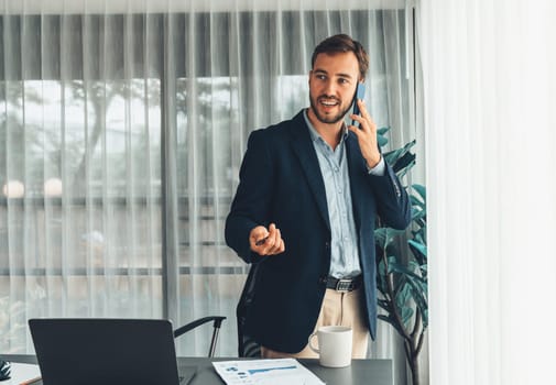 Hardworking businessman stand confidently in modern office making persuasive sales call to client. Office worker talking on the phone coordinate and manage business work with colleagues. Entity