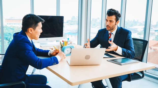 Two business people talk project strategy at office meeting room. Businessman discuss project planning with colleague at modern workplace while having conversation and advice on financial report. Jivy