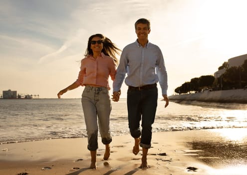 Cheerful Middle Aged Couple Running On The Beach In Summer Time, Happy Mature Man And Woman Holding Hands And Smiling, Husband And Wife Having Fun Together During Date Outdoors, Copy Space