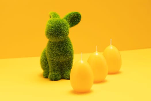 Green Easter Bunny with three yellow candles of eggs shape on matching monochrome orange background. Minimal Happy Easter holiday concept. Creative festive Easter greeting card, copy space for text