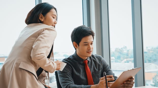 Two business people talk project strategy at office meeting room. Businessman discuss project planning with colleague at modern workplace while having conversation and advice on financial report. Jivy