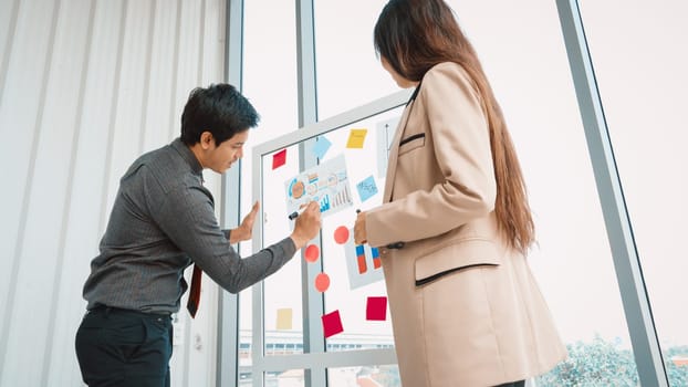 Business people work on project planning board in office and having conversation with coworker friend to analyze project development . They use sticky notes posted on glass to make it organized. Jivy