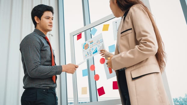 Business people work on project planning board in office and having conversation with coworker friend to analyze project development . They use sticky notes posted on glass to make it organized. Jivy