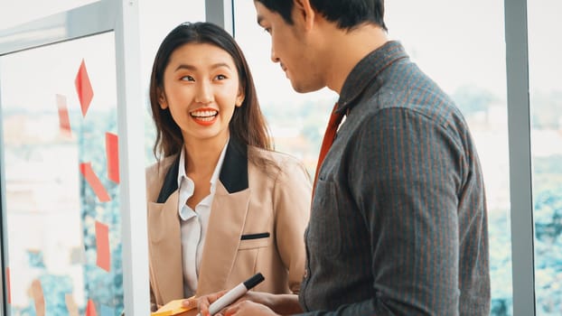 Business people work on project planning board in office and having conversation with coworker friend to analyze project development . They use sticky notes posted on glass to make it organized. Jivy