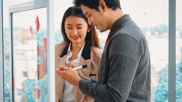 Business people work on project planning board in office and having conversation with coworker friend to analyze project development . They use sticky notes posted on glass to make it organized. Jivy