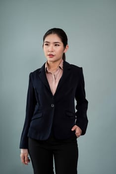 Confident young businesswoman stands on isolated background, posing in formal black suit. Office lady or manager with smart and professional appearance. Enthusiastic