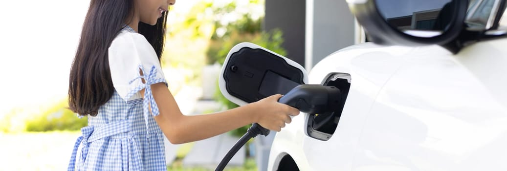 A playful girl holding an EV plug, a home charging station providing a sustainable power source for electric vehicles. Alternative energy for progressive lifestyle.