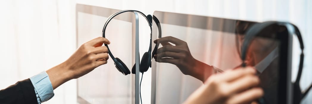 Panorama focus hand holding headset on call center workspace desk with blur background of operator team or telesales representative engaging in providing client with customer support service. Prodigy