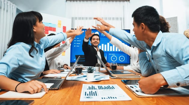 Group of happy multi ethnic businesspeople in celebratory gesture and successful teamwork after made success sales or positive financial data dashboard display on screen in meeting room. Habiliment