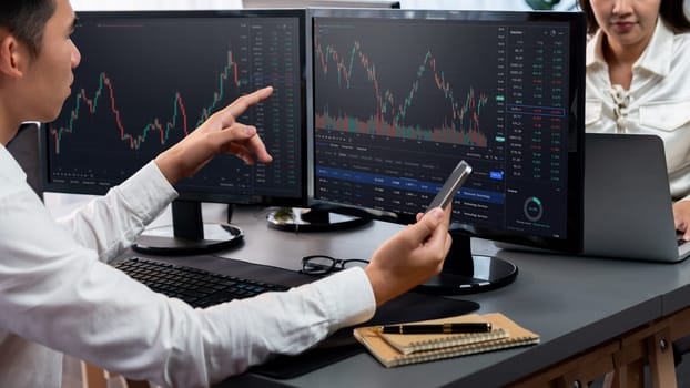 Group of traders discussing on office desk, monitoring stock market on monitor at office workplace. Businessman and broker analyzing stock graph together at stock trading company. Trailblazing