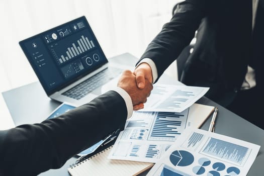 Closeup professional businessman shaking hands over desk in modern office after successfully analyzing pile of dashboard data paper as teamwork and integrity handshake in workplace concept. fervent