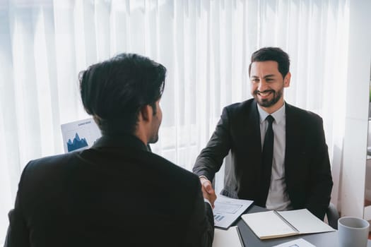 Business partnership meeting with successful trade agreement with handshake or greeting in corporate office desk. Businessman in black suit shaking hand after finalized business deal. Fervent