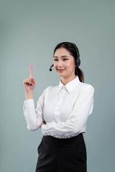 Asian female call center operator with smile face advertises job opportunity, wearing a formal suit and headset pointing finger for product on customizable isolated background. Enthusiastic