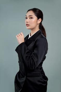 Confident young businesswoman stands on isolated background, posing in formal black suit. Office lady or manager with smart and professional appearance. Enthusiastic