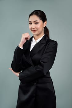 Confident young businesswoman stands on isolated background, posing in formal black suit. Office lady or manager with smart and professional appearance. Enthusiastic