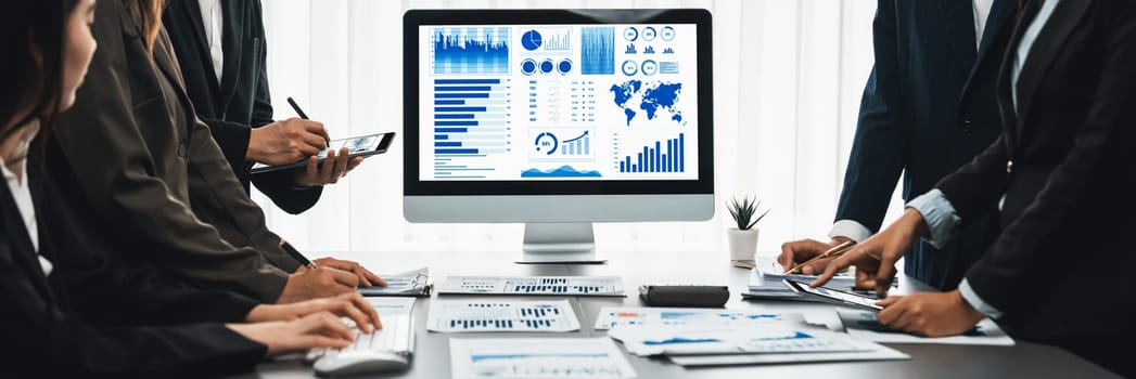 Panorama shot analyst team utilizing BI Fintech to analyze financial report with laptop. Businesspeople analyzing BI data dashboard displayed on laptop screen for business insight. Prodigy