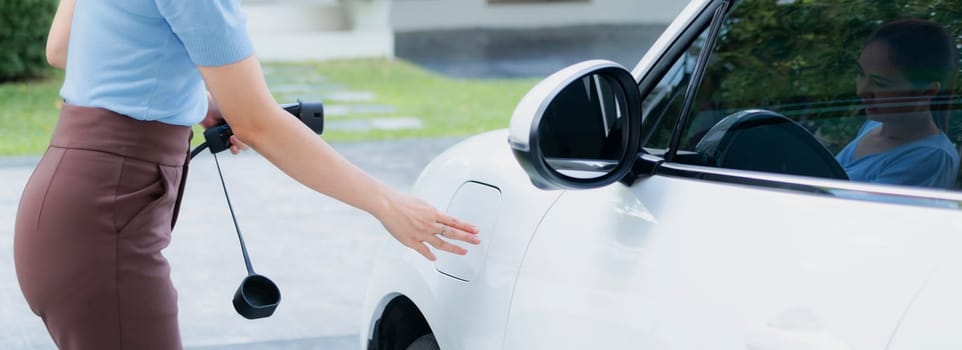 Closeup progressive woman install cable plug to her electric car with home charging station. Concept of the use of electric vehicles in a progressive lifestyle contributes to clean environment.