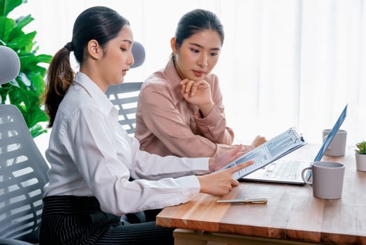 Two young office lady colleagues collaborating in modern office workspace, engaging in discussion and working together on laptop, showcasing their professionalism as modern office worker. Enthusiastic