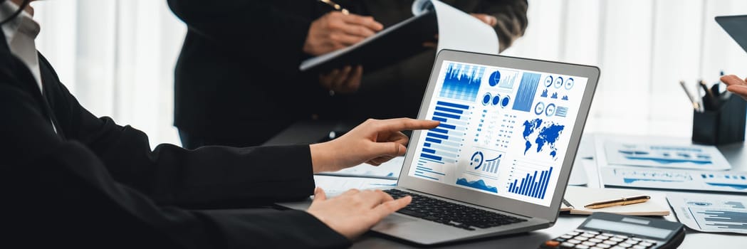 Panorama shot analyst team utilizing BI Fintech to analyze financial report with laptop. Businesspeople analyzing BI data dashboard displayed on laptop screen for business insight. Prodigy