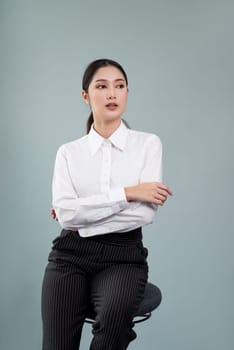 Confident young businesswoman sitting on a chair on isolated background, posing in formal black suit. Successful office lady or manager with smart and professional appearance. Enthusiastic