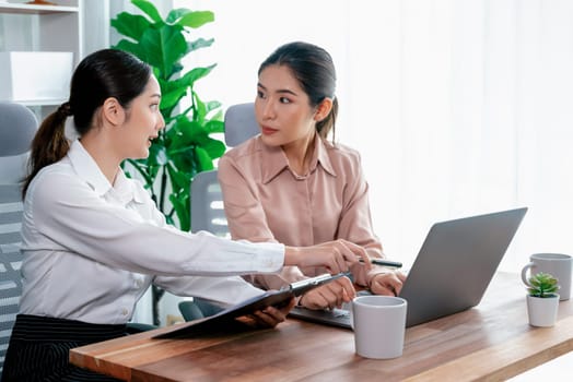 Two young office lady colleagues collaborating in modern office workspace, engaging in discussion and working together on laptop, showcasing their professionalism as modern office worker. Enthusiastic