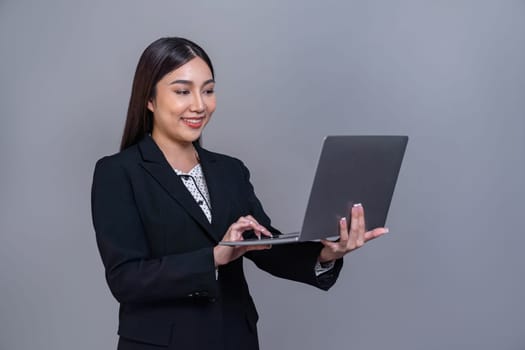 Confident young Asian businesswoman posing with laptop on isolated background. Office lady make hand holding gesture for promotions sales, technology advertisements or HR recruitment image. Jubilant