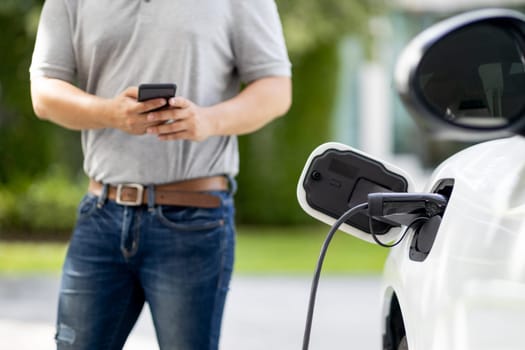 Progressive asian man install cable plug to his electric car with home charging station in the backyard. Concept use of electric vehicles in a progressive lifestyle contributes to clean environment.