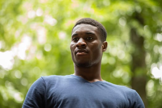 Portrait African American Young Sportive Man On Green Park on Background, Handsome Male Looks Away, Serious Face Expression. Low Angle, Outdoor. Horizontal Plane. Copy Space For Text