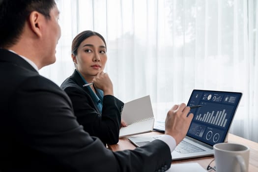 Busy analyst team in office discuss data analysis and marketing strategy using BI dashboard and statistics on laptop screen to improve business performance at meeting with strong teamwork. Jubilant