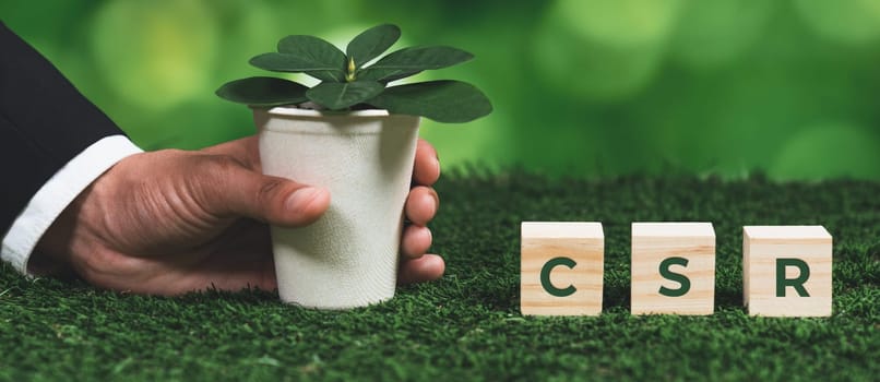 Businessman holding plant pot with cube symbolizing CSR. Ethical and eco-friendly green business with no CO2 emission policy. Committed to corporate social responsibility for greener community. Alter