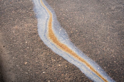 After a rain, a spreading stain of oil or gasoline on the asphalt. Close up abstract background