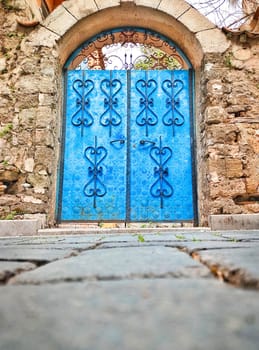 Blue old gate with patterned forging on background of facade of old masonry wall, lower viewing angle