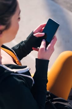 vertical close up top view of an unrecognizable sportive woman using a mobile phone, concept of technology of communication and urban sports