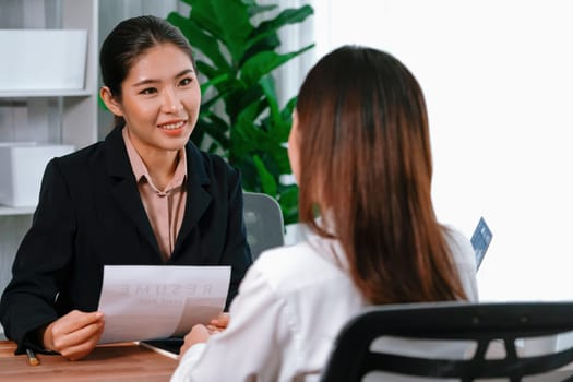 Two asian women conduct job interview in office. Applicants wear formal suit while talking about her CV and job application. Interviewer ask inquiry in positive and conversational manner. Enthusiastic