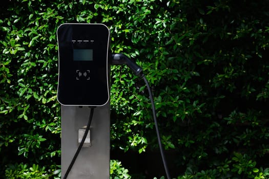 Charging station with greenery foliage background for combination of nature and alternative energy for progressive future renewable energy for electric car. Charger point with connecter device.