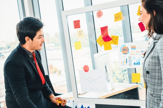 Business people work on project planning board in office and having conversation with coworker friend to analyze project development . They use sticky notes posted on glass to make it organized. Jivy