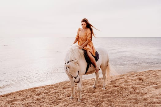 A woman in a dress stands next to a white horse on a beach, with the blue sky and sea in the background