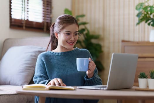 Young asian relaxed smiling pretty woman relaxing with laptop at home. Female feeling joy enjoying with mobile phone on cozy couch.