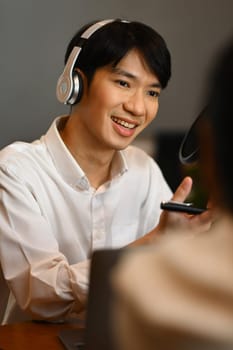 Smiling radio host wearing headphone and recording voice over radio interview guest conversation at home studio.