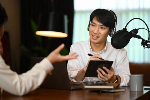 Friendly female radio host discussing various topics with her guest while streaming live audio podcast from home studio.