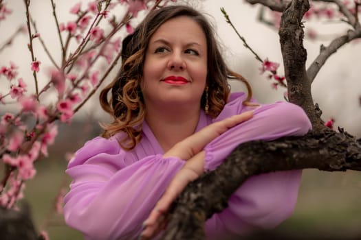 Woman peach blossom. Happy curly woman in pink dress walking in the garden of blossoming peach trees in spring.