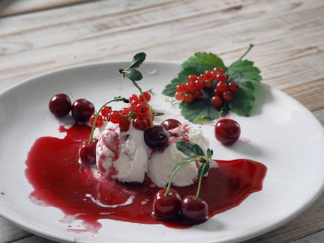 Red cherries and red currants on ice cream with jam in a white plate on a white wooden table.Food background